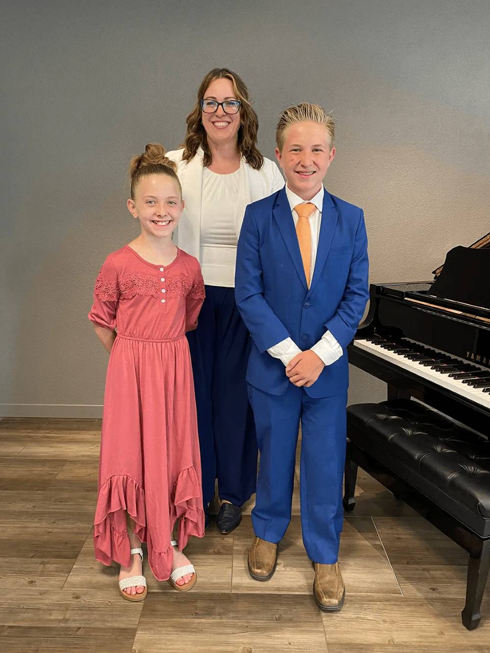 Jennifer Jackson with two students dressed for a recital beside the studio's grand piano